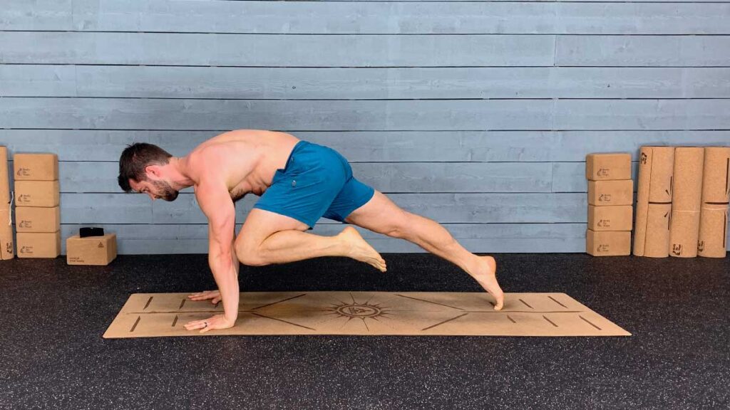 Shirtless Male Yoga Instructor Demonstrates Downward Facing Dog Knee to Elbow Pose