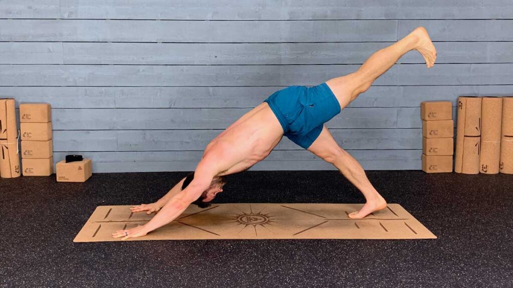 Shirtless Male Yoga Instructor Demonstrates Downward Facing Dog Pose With Leg Extended