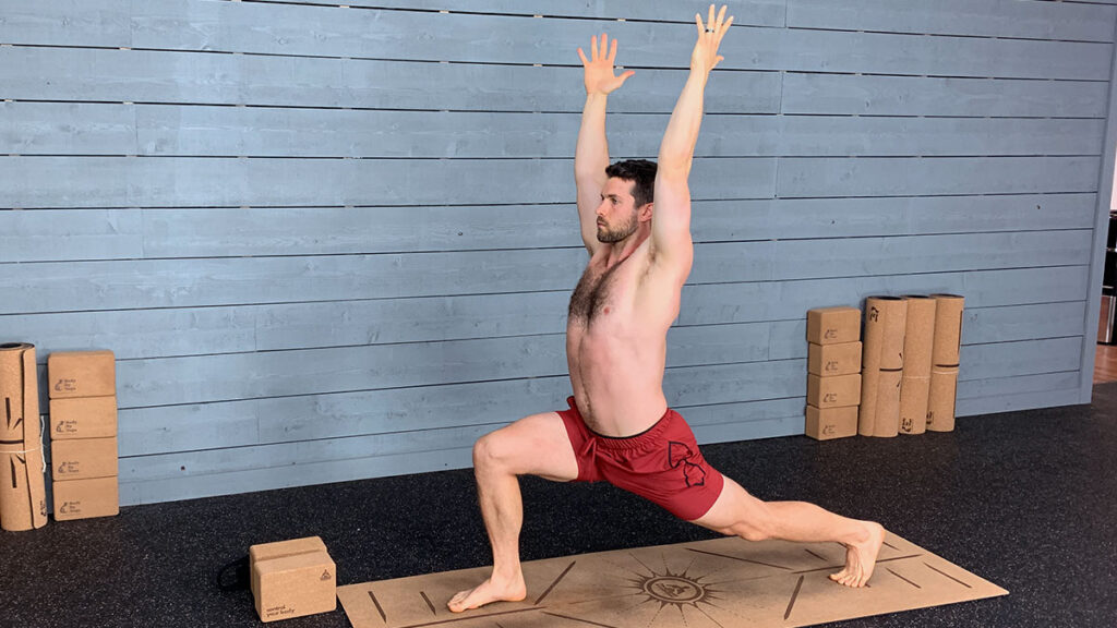 shirtless male yoga instructor demonstrates high lunge pose with arms up as part of morning yoga routine