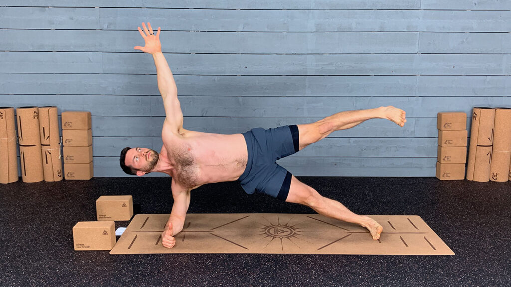 shirtless male yoga instructor demonstrates side plank leg raised pose as part of morning yoga routine
