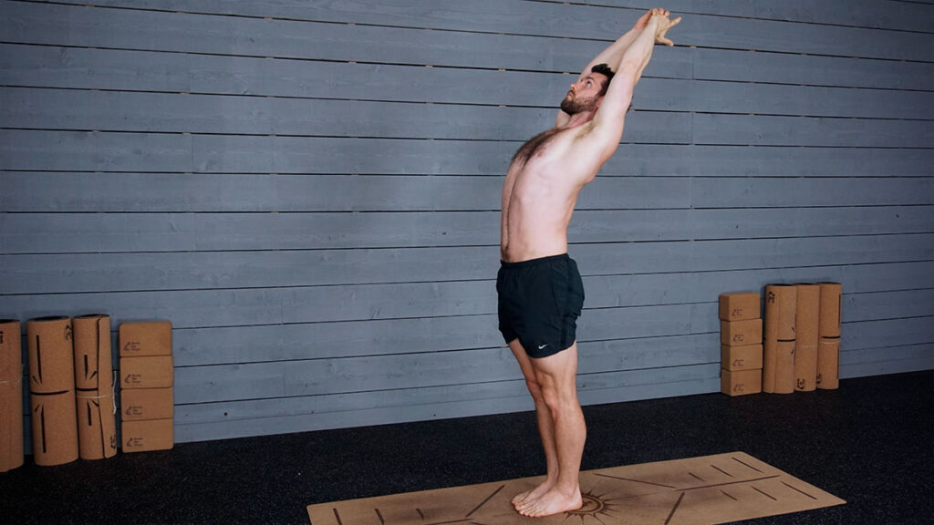 Shirtless male yoga instructor demonstrates standing back bend pose as part of morning yoga routine