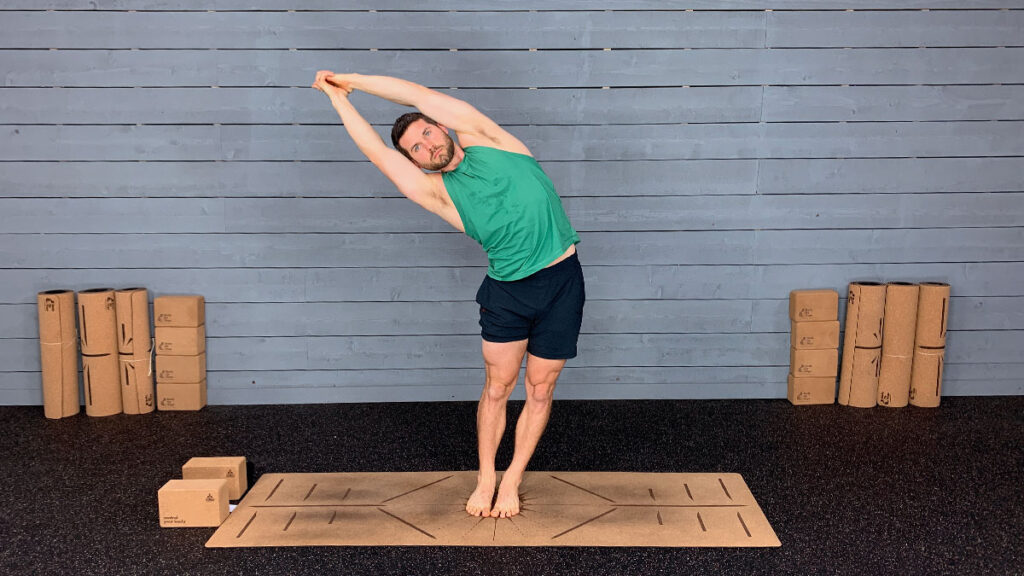 Male yoga instructor demonstrates standing side bend as part of morning yoga routine