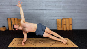 Shirtless male yoga instructor demonstrates side plank on mat