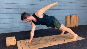 Male yoga instructor demonstrates one arm plank pose on yoga mat