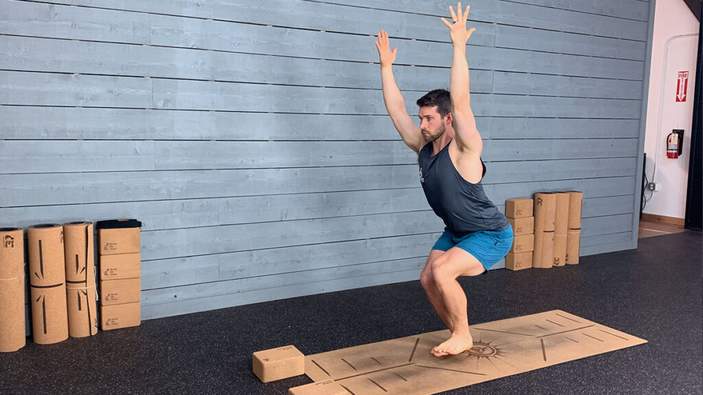 male yoga instructor demonstrates single leg chair pose
