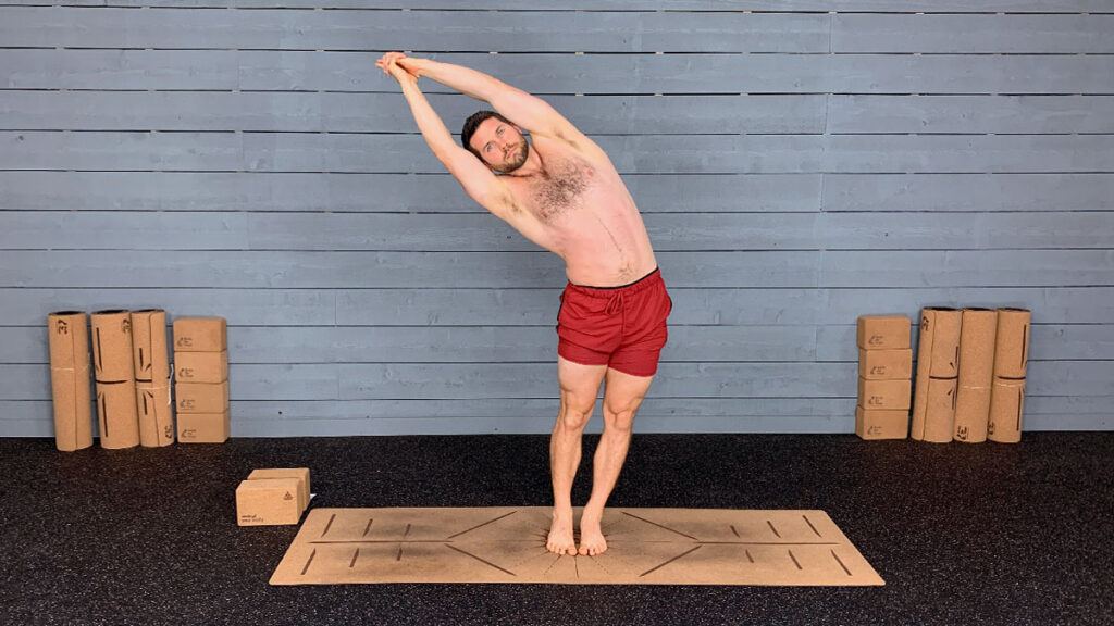 Shirtless male yoga instructor demonstrates standing side bend pose