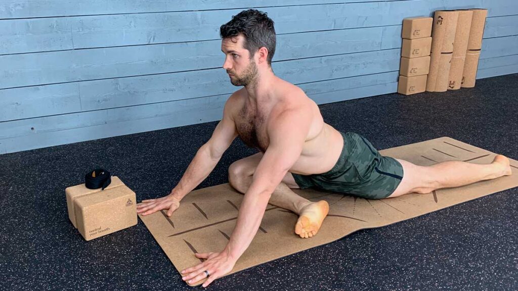 Shirtless male yoga instructor demonstrating yoga exercises for hips including pigeon pose