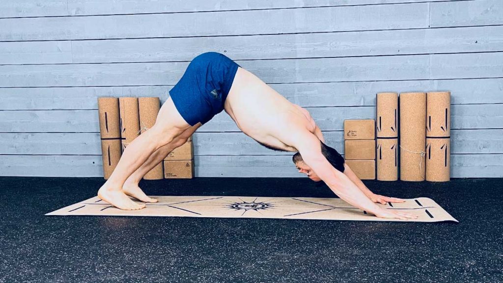Shirtless male yoga instructor demonstrates down dog pose