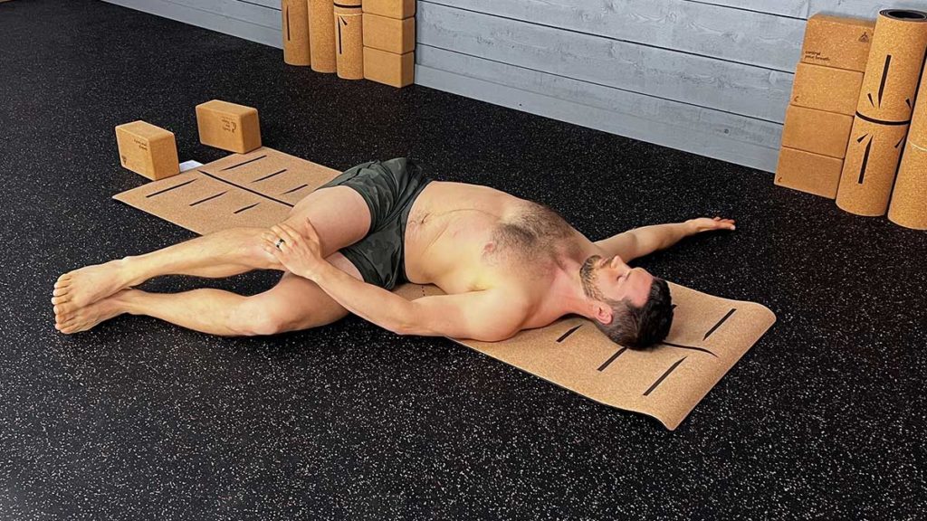 shirtless male yoga instructor demonstrates reclined twist pose