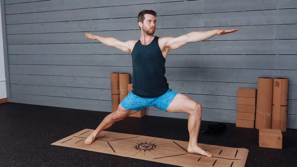 Male yoga instructor demonstrates warrior 2 pose
